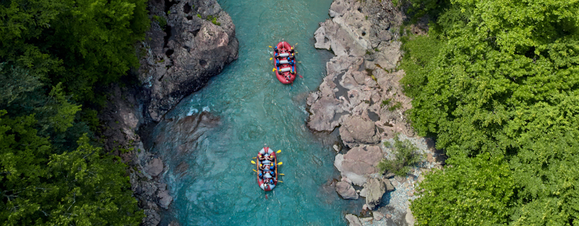 Twee boten met mensen die op een rafting excursie zijn van bovenaf. De rivier loopt in de afbeelding van beneden naar boven. Aan weerskanten een stenen oever en daarachter de bebossing.