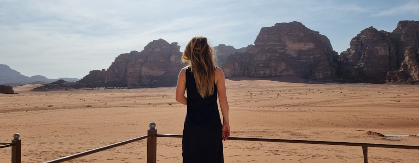 Vrouw van de achterkant in wadi rum kijkend naar rotsen en zandvlakte