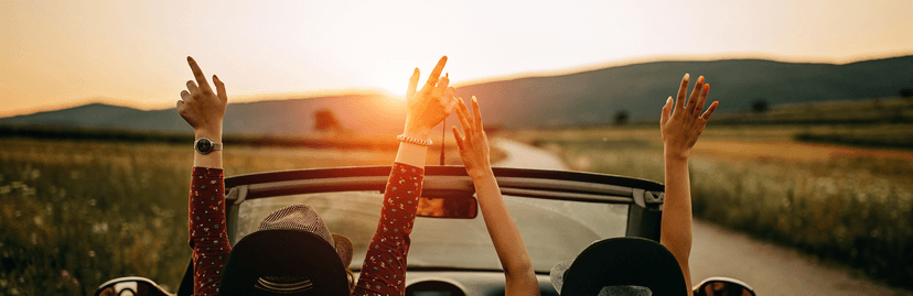 Meisjes met armen in de lucht in een auto met open dak en zonsondergang achter de bergen