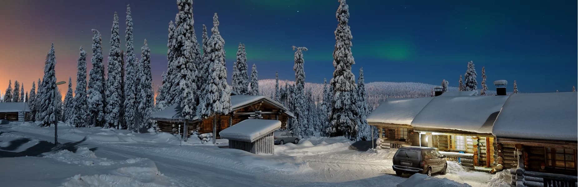 Snow-covered cabins and cars surrounded by snowy trees under a night sky with a faint aurora borealis.