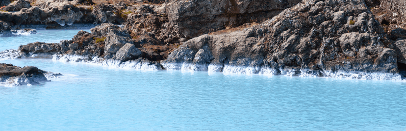 Het felblauwe water van de Blue Lagoon met groene bergen en wolken erachter