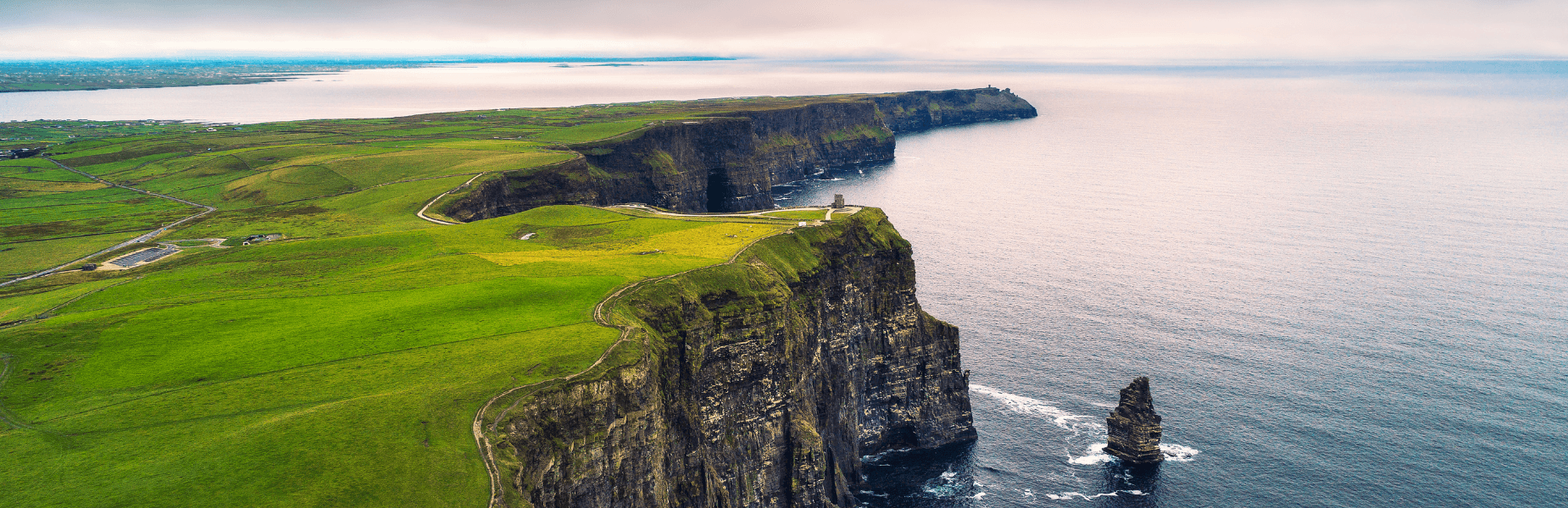 Aerial view of the Cliffs of Moher, Ireland, with lush green fields atop steep cliffs overlooking the vast Atlantic Ocean.