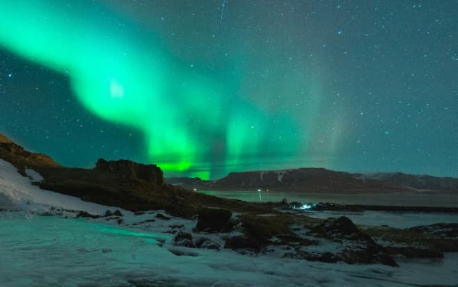 Noorderlicht in IJsland, groen en blauwe licht met sneeuw op de grond en bergen op de achtergornd