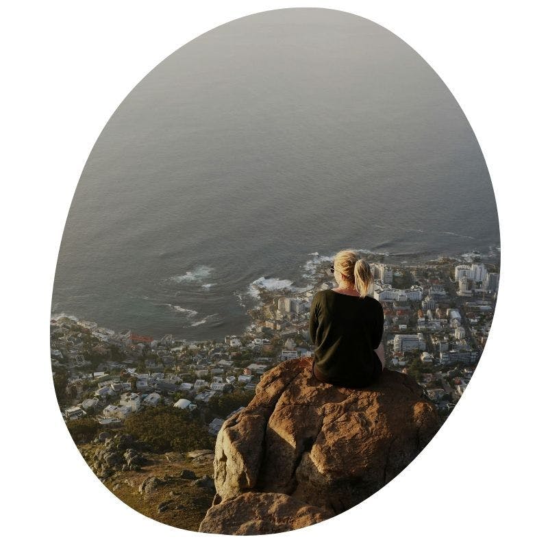 Vrouw die op een rots zit en uitkijkt over Camps Bay