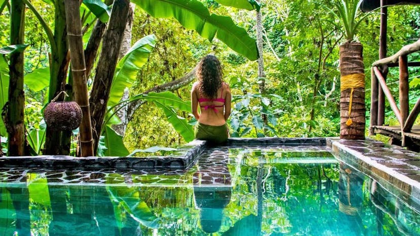 Meisje zittend op de rand van een zwembad met uitzicht de jungle in