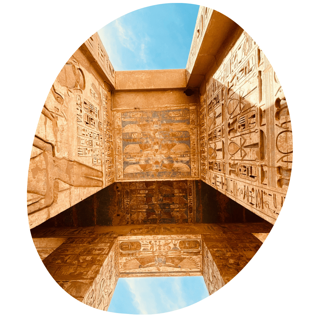 Looking up at an ancient Egyptian temple's intricately carved stone ceiling and walls, with clear blue sky visible above.