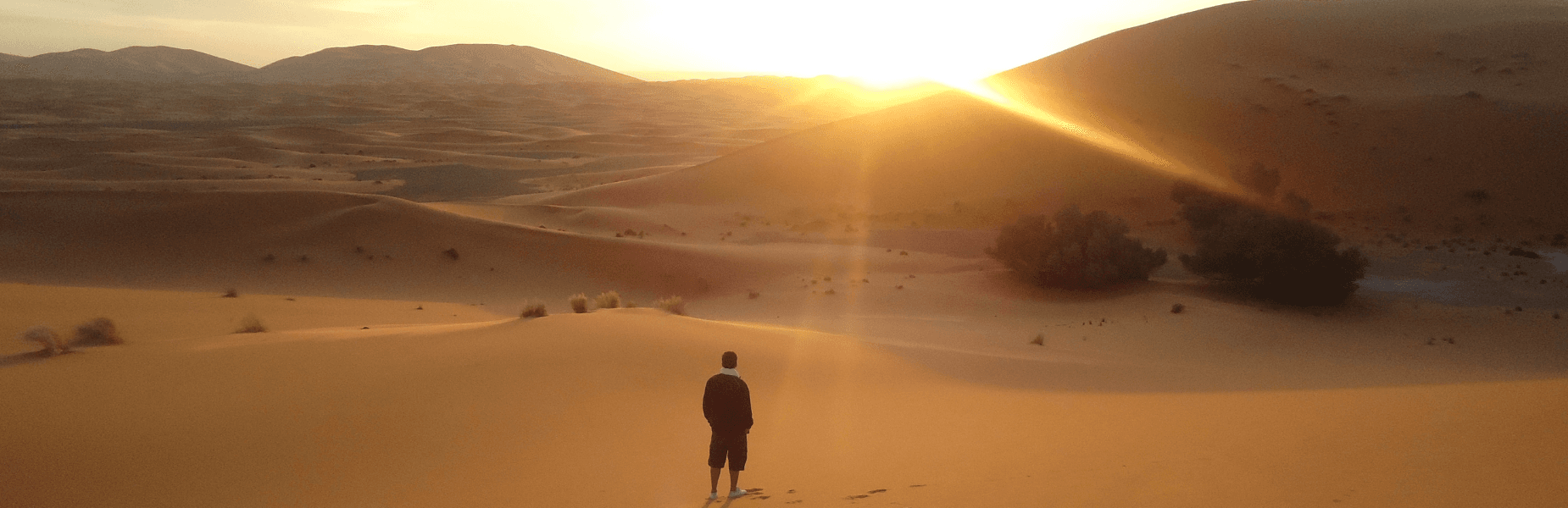 Een man in het zwart in de woestijn met ondergaande zon