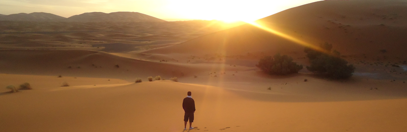Een man in het zwart in de woestijn met ondergaande zon