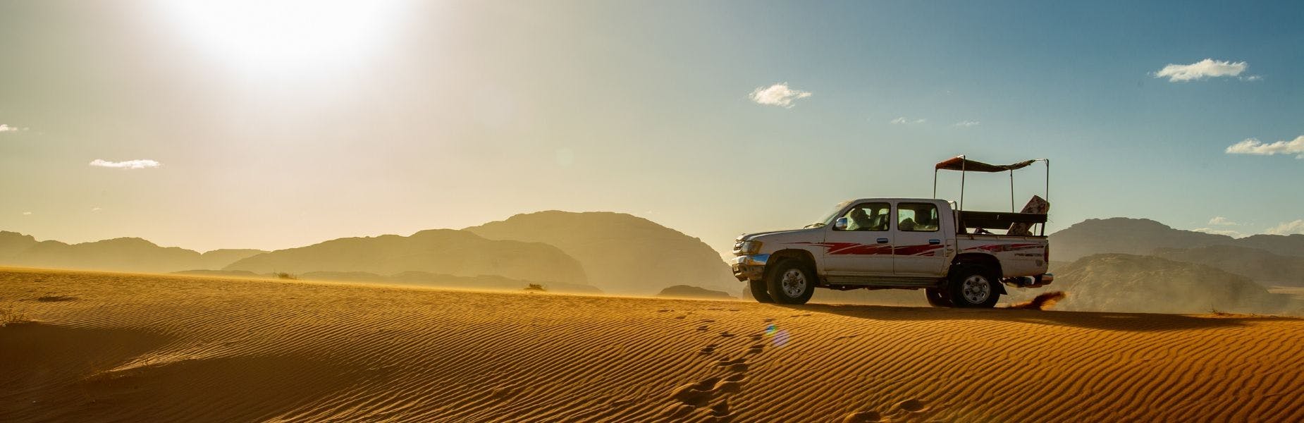Auto op een zandduin in de woestijn met berglandschap op de achtergrond