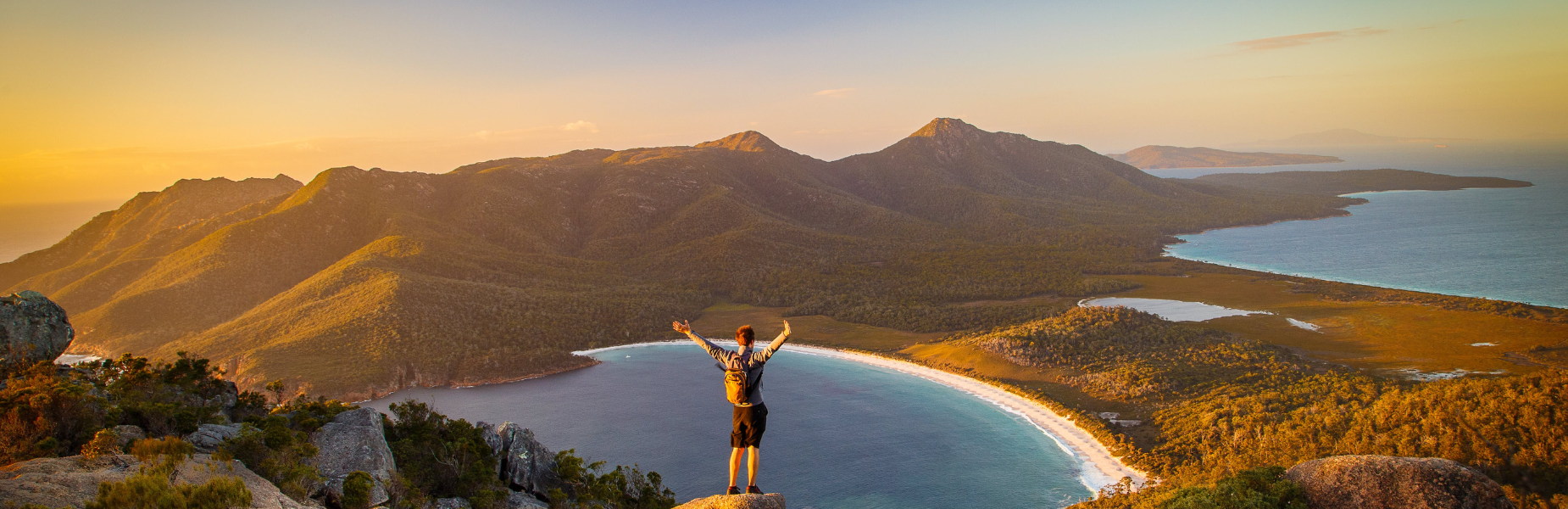 Een jongen met zijn armen in de lucht op een bergtop kijkend naar bergen en de zee