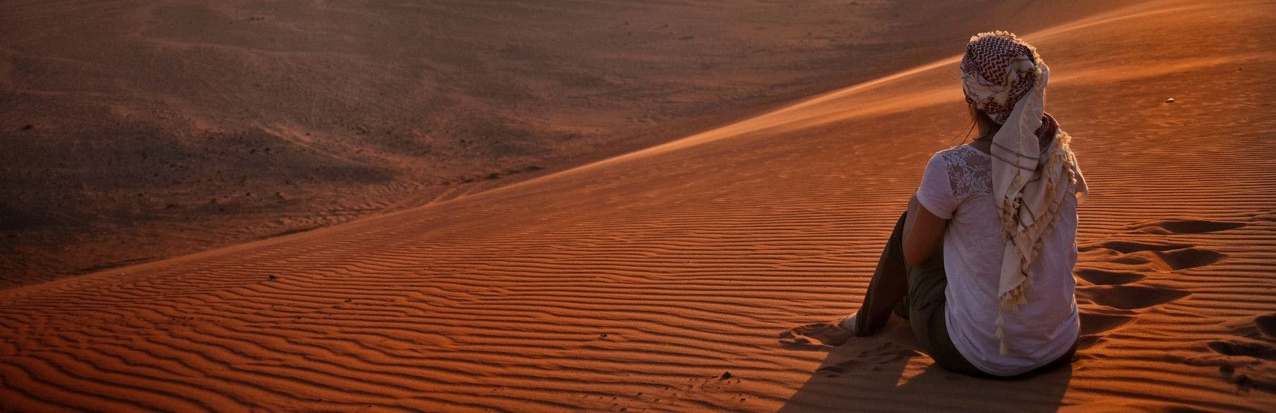 persoon vanaf de achterkant zittend in de woestijn Jordanië